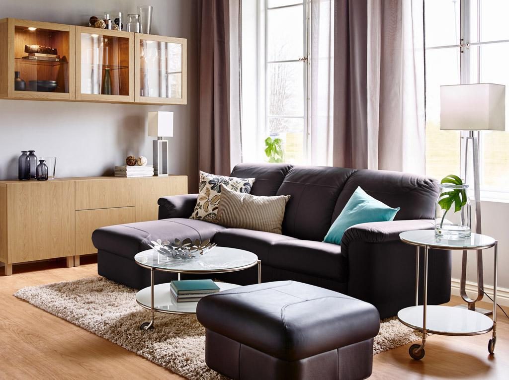 Warm living room with a dark leather chaise sofa, oak wall cabinets, glass side tables and a floor lamp